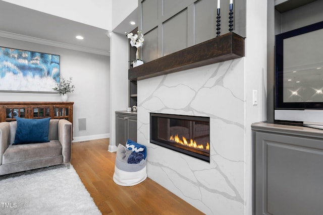 living room featuring light wood finished floors, baseboards, a glass covered fireplace, crown molding, and recessed lighting