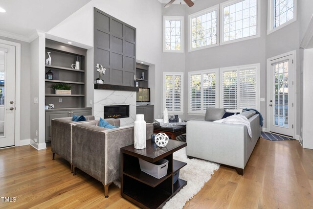 living room featuring built in shelves, a high end fireplace, a healthy amount of sunlight, and light wood-style flooring