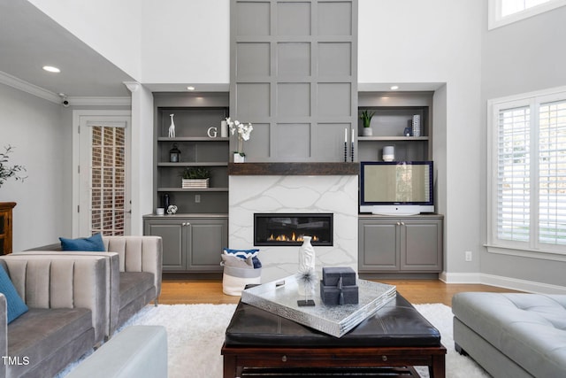 living area with built in shelves, crown molding, a high end fireplace, light wood-type flooring, and baseboards