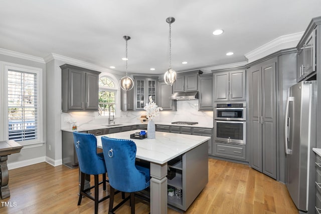 kitchen with glass insert cabinets, a center island, stainless steel appliances, under cabinet range hood, and a sink