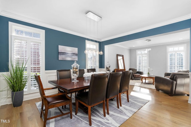 dining area with an inviting chandelier, wainscoting, light wood-style flooring, and crown molding