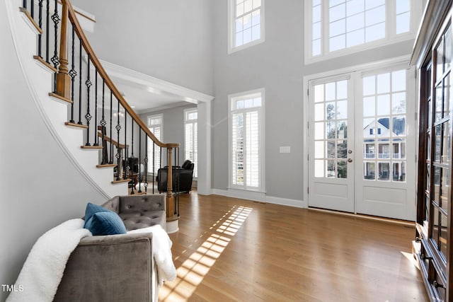 foyer entrance with baseboards, light wood-style flooring, stairway, a high ceiling, and french doors