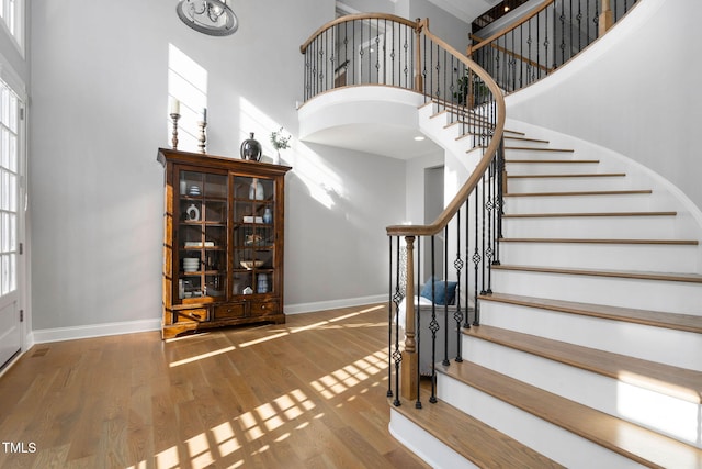 foyer featuring a towering ceiling, stairway, baseboards, and wood finished floors