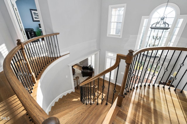 stairs with baseboards, a high ceiling, a chandelier, and wood finished floors