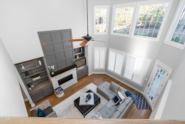 living room with a towering ceiling, ceiling fan, baseboards, and wood finished floors