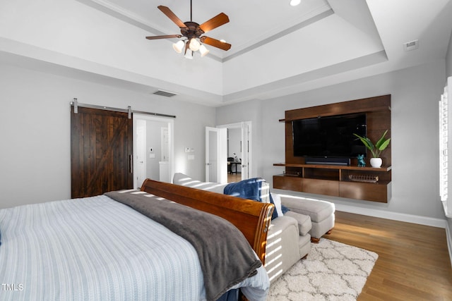 bedroom featuring wood finished floors, a barn door, a raised ceiling, and visible vents