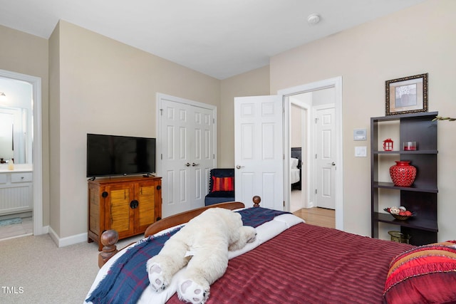 bedroom featuring a closet, light carpet, connected bathroom, and baseboards