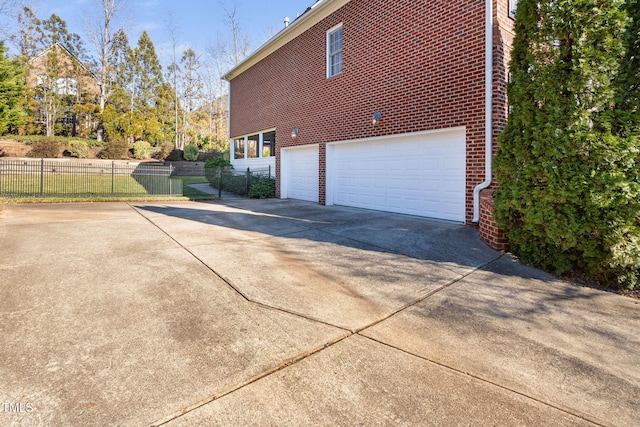 view of side of home featuring a garage, fence, concrete driveway, and brick siding