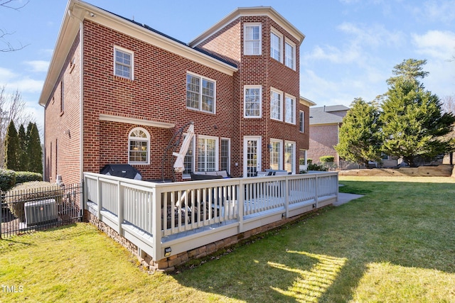 back of property featuring brick siding, a lawn, a deck, and fence