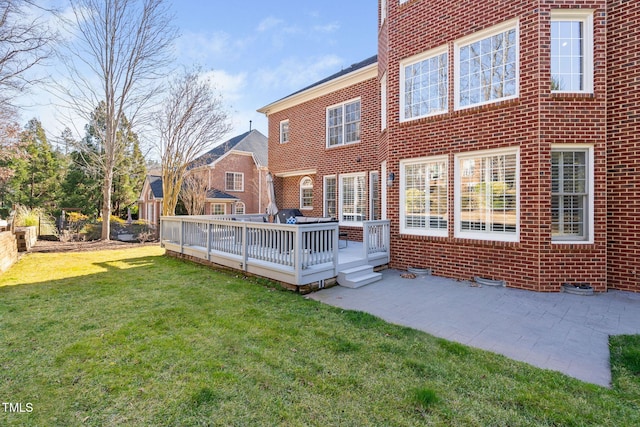 rear view of house featuring a deck, a yard, brick siding, and a patio