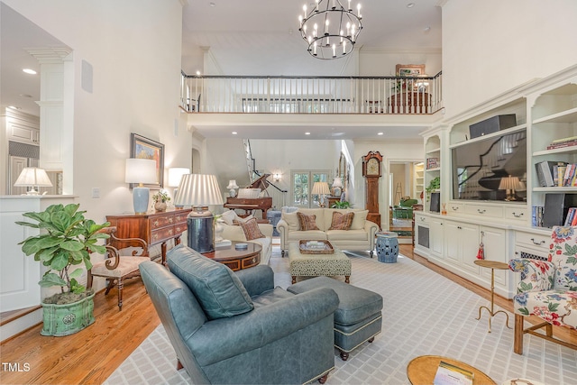 living room featuring crown molding, light wood-type flooring, a towering ceiling, and a notable chandelier