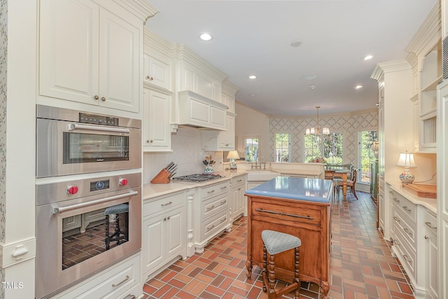 kitchen with pendant lighting, brick floor, light countertops, appliances with stainless steel finishes, and wallpapered walls