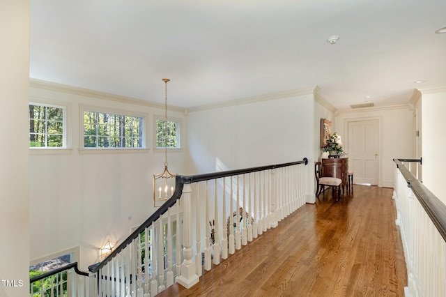 hall with visible vents, wood finished floors, an inviting chandelier, crown molding, and an upstairs landing