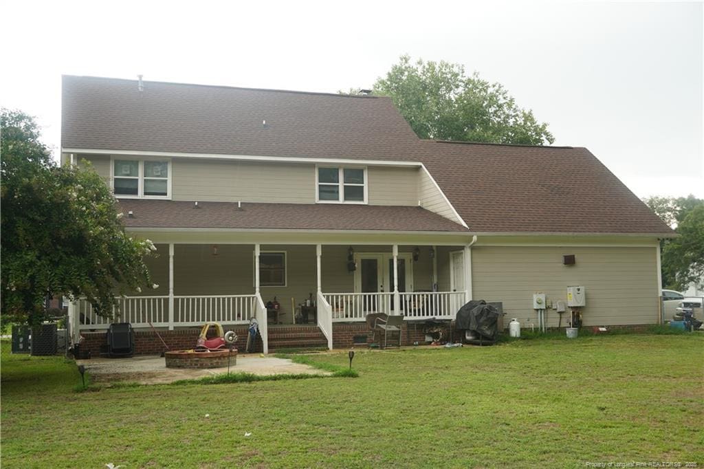 rear view of house featuring a porch, a patio area, a yard, and roof with shingles