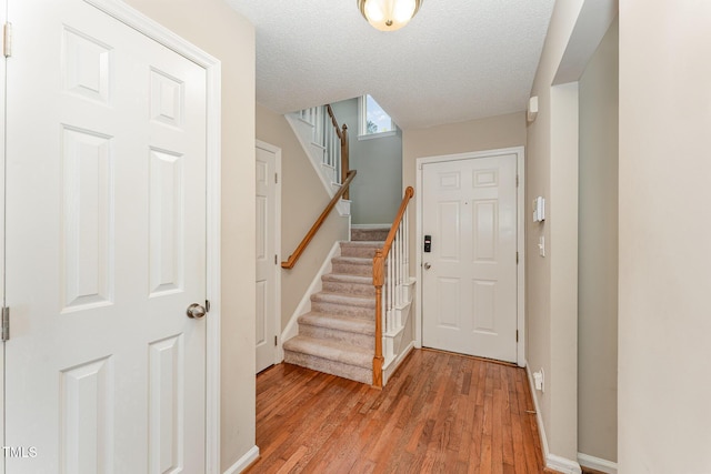 foyer featuring light wood finished floors, stairs, baseboards, and a textured ceiling