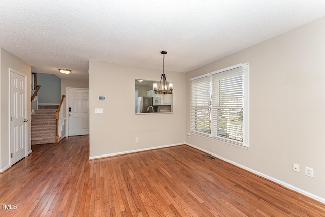 empty room with a chandelier, visible vents, baseboards, light wood-style floors, and stairway