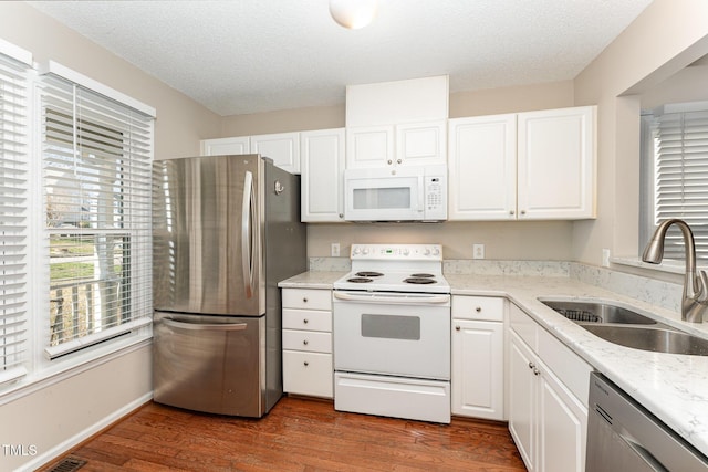 kitchen with stainless steel appliances, dark wood finished floors, white cabinetry, and a sink