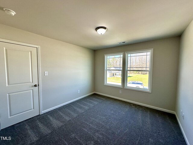 spare room with visible vents, baseboards, and dark colored carpet