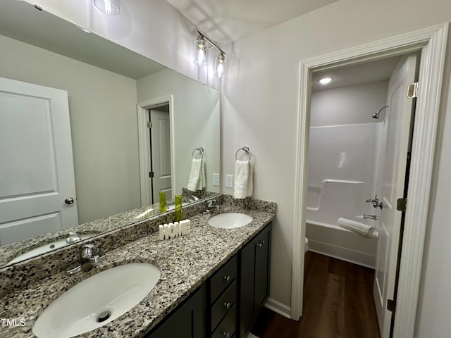 bathroom with double vanity, shower / washtub combination, wood finished floors, and a sink