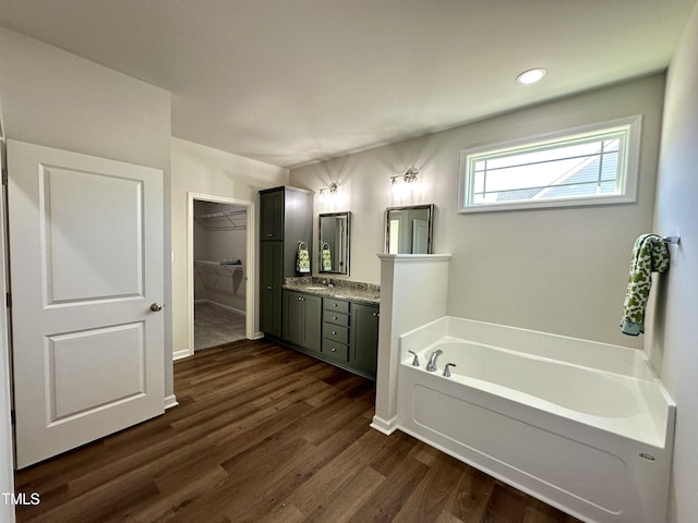 bathroom with vanity, a garden tub, a spacious closet, and wood finished floors