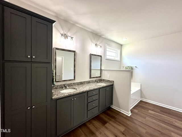 full bath featuring wood finished floors, baseboards, double vanity, a sink, and a bath