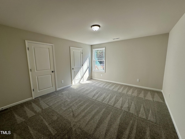 empty room with carpet, visible vents, and baseboards