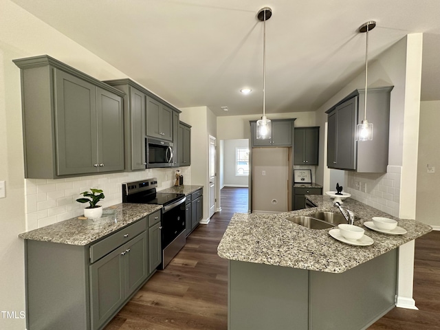 kitchen with light stone counters, a peninsula, a sink, dark wood-type flooring, and appliances with stainless steel finishes