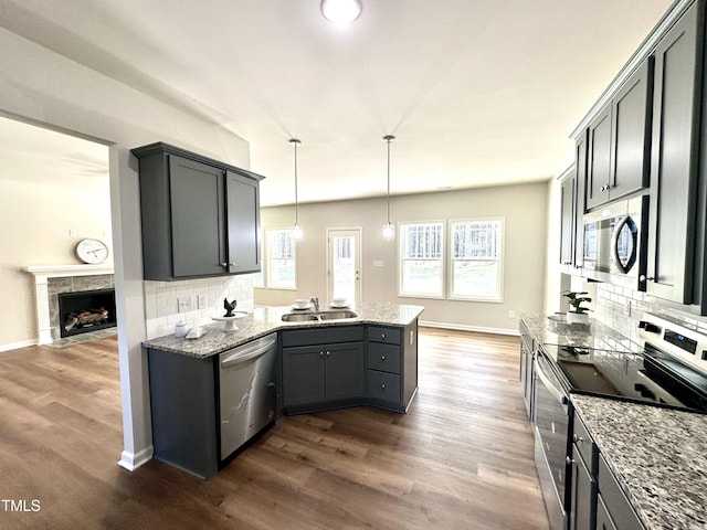 kitchen featuring a sink, decorative backsplash, a peninsula, stainless steel appliances, and dark wood-style flooring