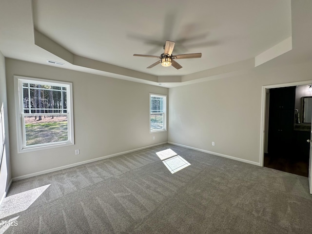 carpeted empty room featuring a tray ceiling, visible vents, baseboards, and a ceiling fan