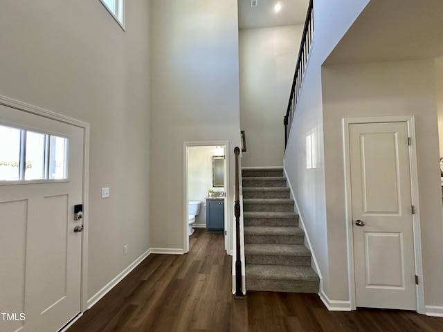 entryway with dark wood-style floors, stairway, baseboards, and a towering ceiling