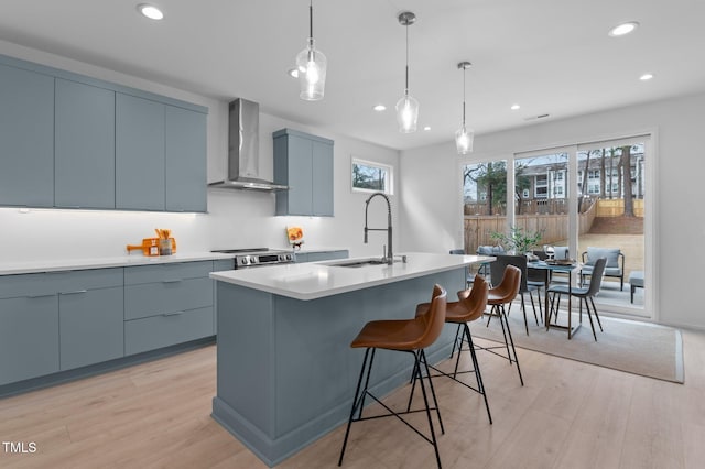 kitchen with light wood-style floors, wall chimney exhaust hood, light countertops, and a sink