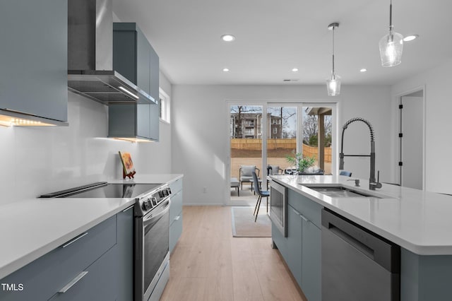 kitchen featuring light countertops, appliances with stainless steel finishes, a kitchen island with sink, a sink, and wall chimney exhaust hood