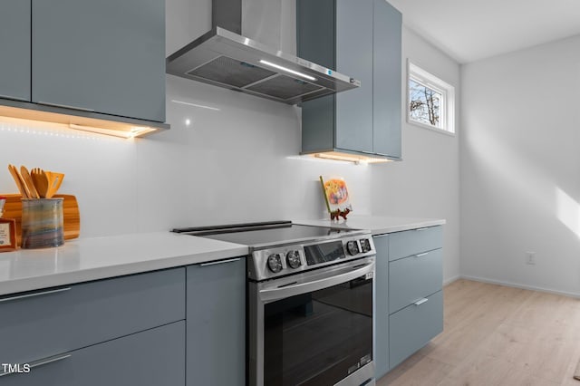 kitchen featuring wall chimney range hood, stainless steel electric stove, gray cabinets, and light countertops