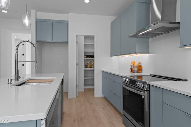 kitchen with electric range, wall chimney exhaust hood, light countertops, light wood-style floors, and a sink