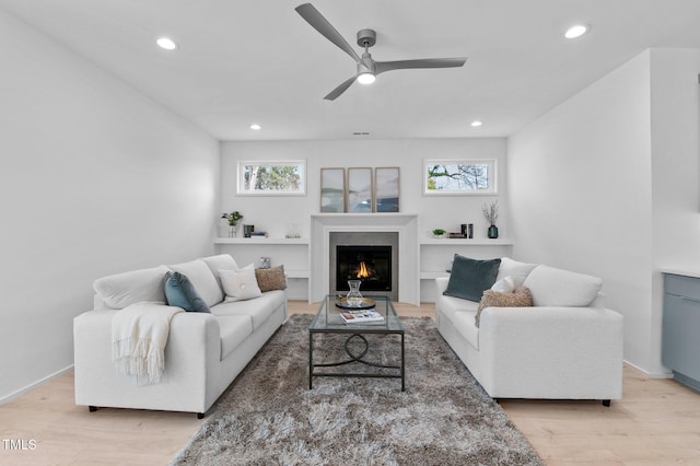 living room with a warm lit fireplace, recessed lighting, plenty of natural light, and light wood-style floors