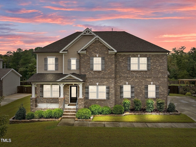 view of front of house with covered porch, brick siding, a yard, and concrete driveway