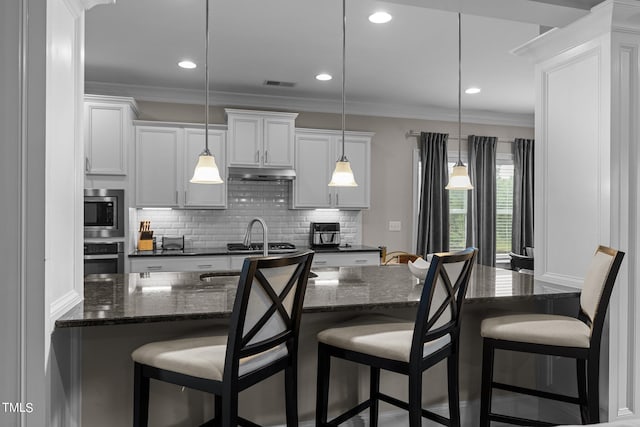 kitchen with under cabinet range hood, white cabinetry, a breakfast bar area, and decorative light fixtures