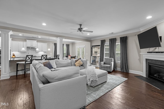 living room featuring decorative columns, dark wood-type flooring, and a glass covered fireplace