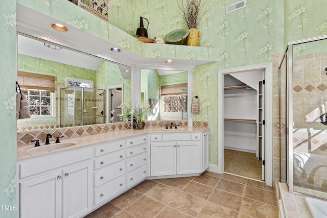 full bath with a sink, visible vents, a shower stall, double vanity, and wallpapered walls