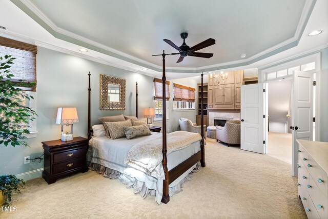 bedroom with ornamental molding, a tray ceiling, light carpet, and a fireplace