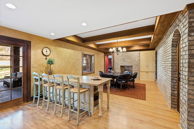 kitchen featuring an inviting chandelier, light wood-style flooring, brick wall, and beam ceiling