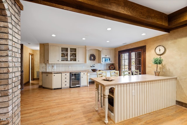 kitchen with light wood finished floors, beamed ceiling, wine cooler, and stainless steel microwave