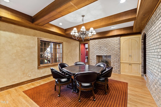 dining space with light wood-type flooring, a notable chandelier, beamed ceiling, and a fireplace