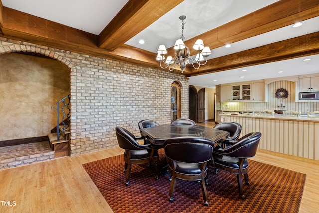 dining space with arched walkways, beam ceiling, brick wall, and wood finished floors