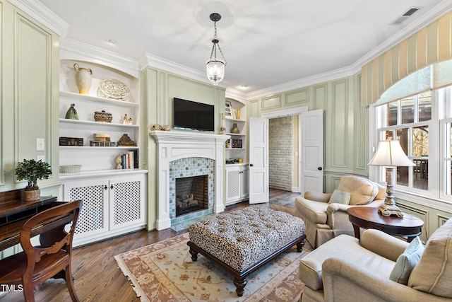 living room with wood finished floors, a tile fireplace, built in features, and crown molding