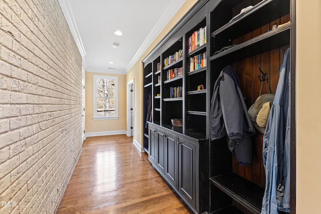 corridor with light wood-style floors, brick wall, ornamental molding, and baseboards