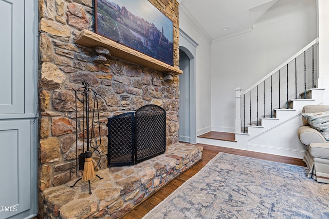 living room with arched walkways, wood finished floors, stairs, crown molding, and a stone fireplace