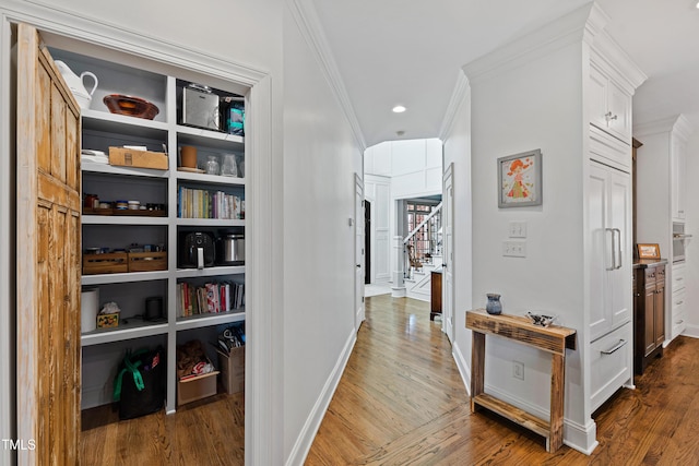 corridor featuring recessed lighting, wood finished floors, baseboards, stairs, and ornamental molding