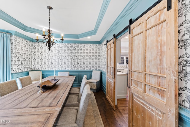 dining space with a barn door, a raised ceiling, dark wood-type flooring, an inviting chandelier, and crown molding