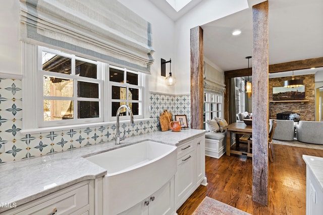 kitchen with a fireplace, a sink, white cabinetry, light stone countertops, and dark wood-style floors